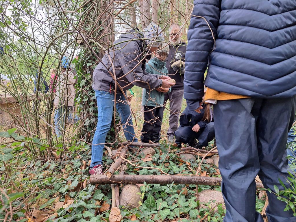 Der Umriss der Schlafhütte wurde mit Steinen und Ästen markiert. Doris erklärt welche Steine als nächstes gebraucht werden.